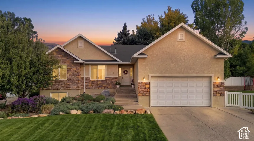 Exterior featuring a stone and stucco facade, an attached garage, a manicured lawn, and established landscaping