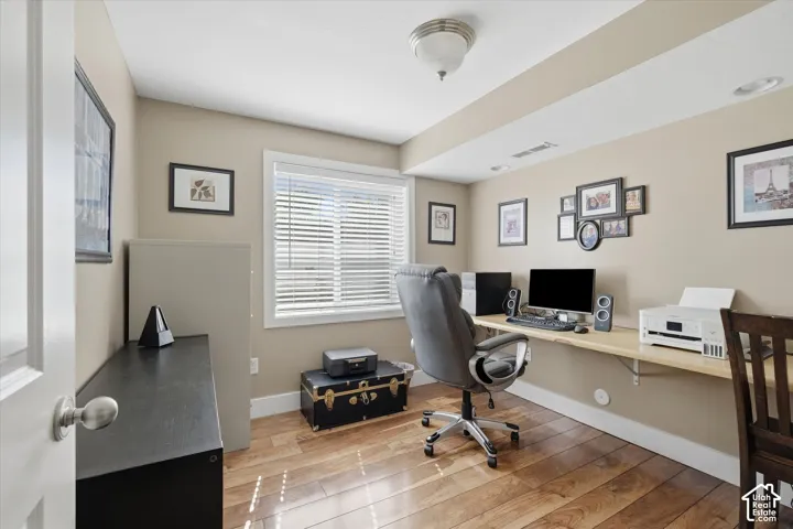 Room featuring wood-finish flooring, a built-in wood desktop, and a window with blinds