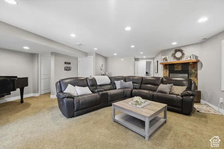 Recessed lighting throughout, carpeted flooring, and a stone-clad fireplace with a wood mantle