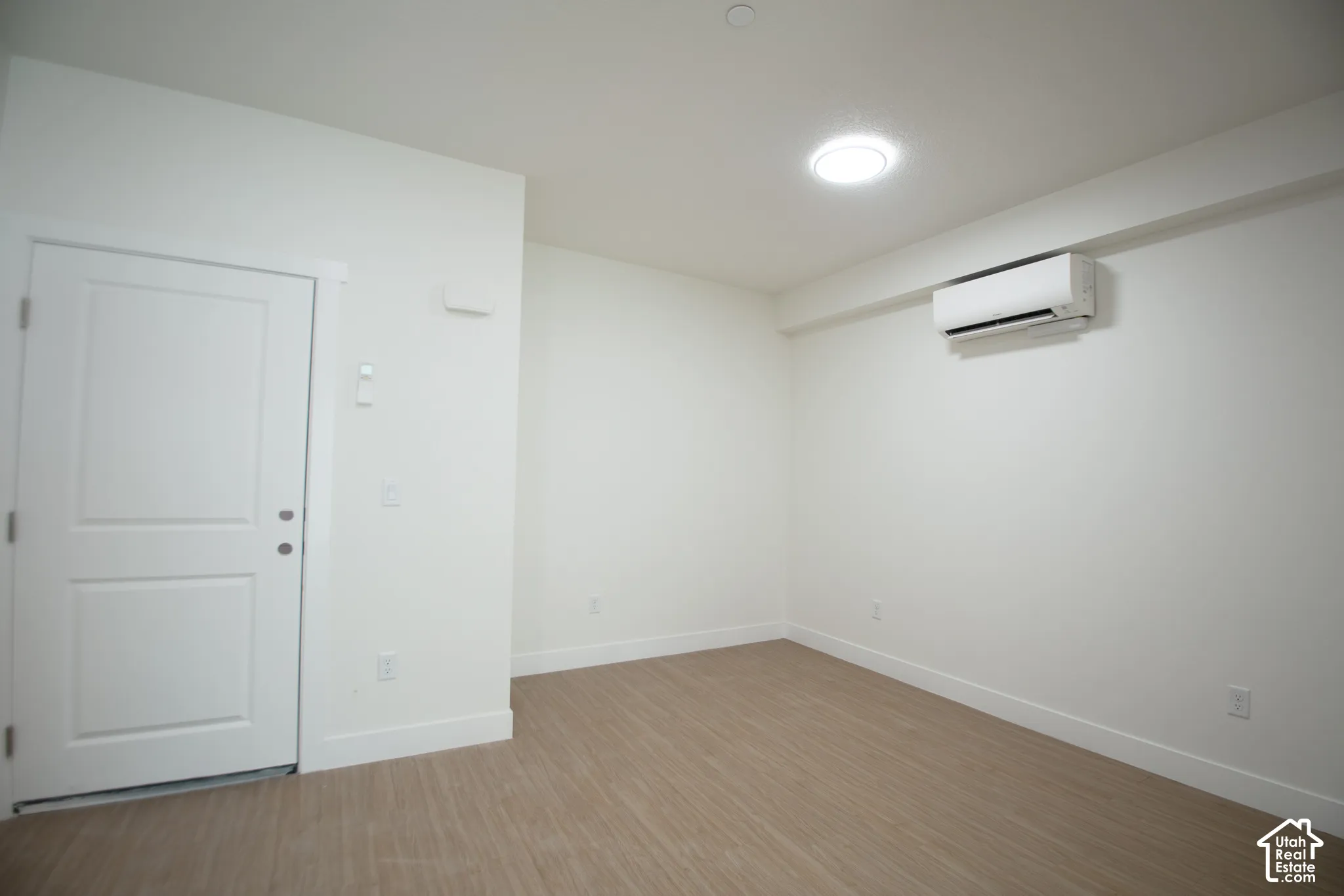 Recessed ceiling lighting, wood-finish flooring, white trim, and a wall-mounted climate control unit