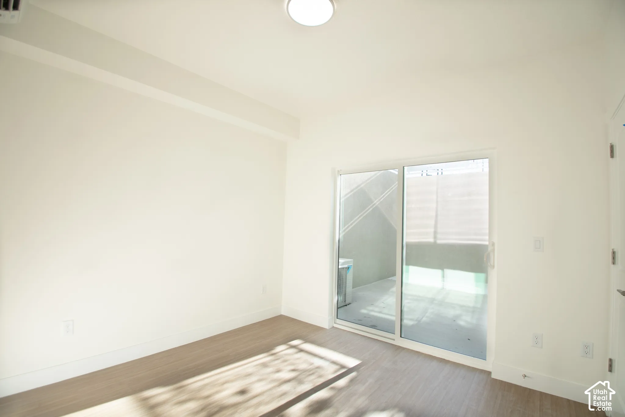 Sliding glass door, wood-finish flooring, recessed lighting, and crisp white walls