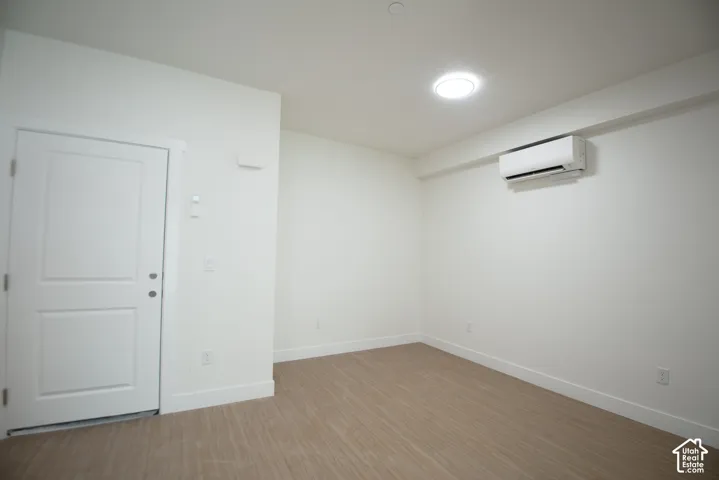 Recessed ceiling lighting, wood-finish flooring, white trim, and a wall-mounted climate control unit