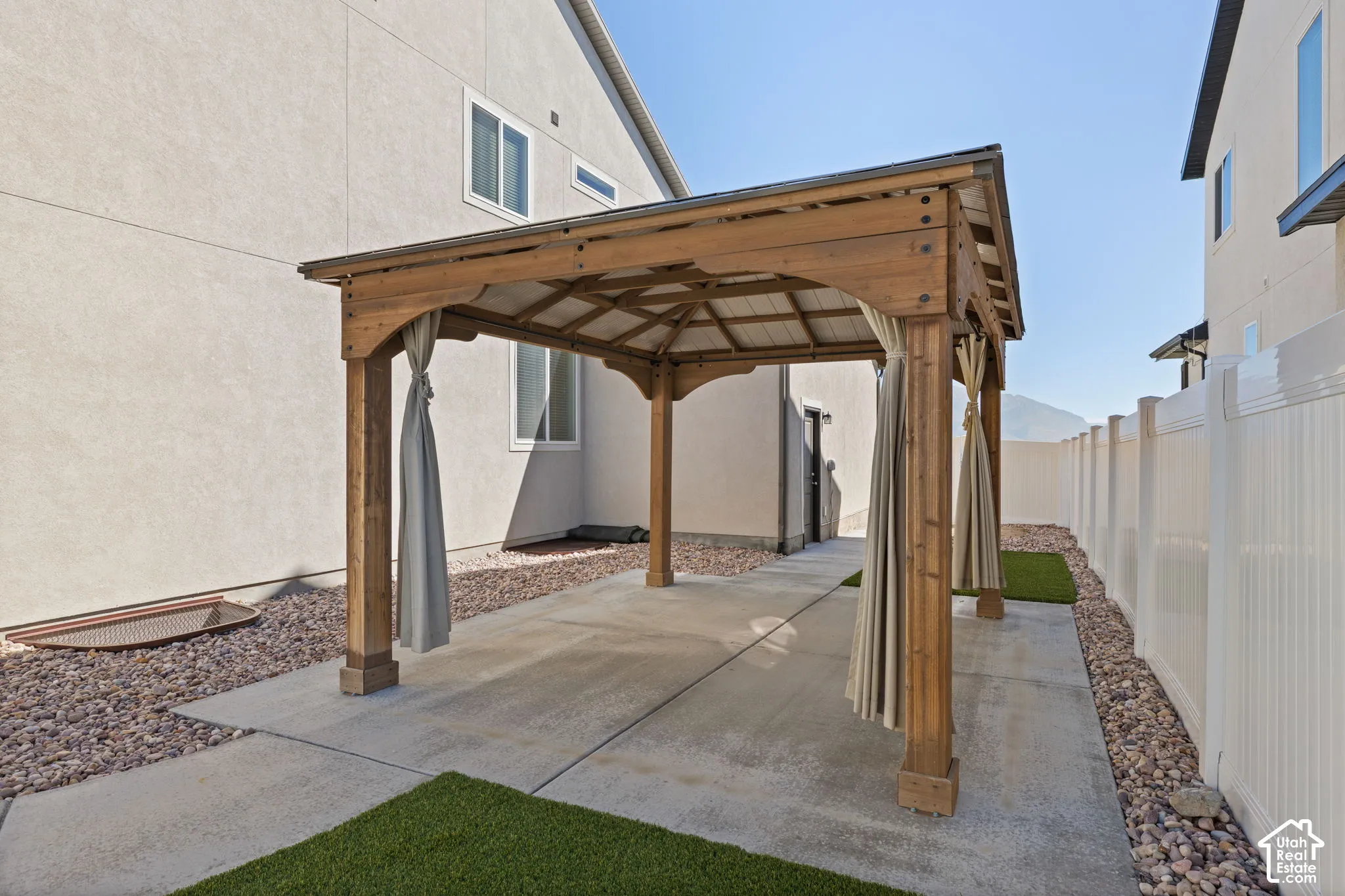 Wood gazebo with draped privacy screens, concrete patio area, and gravel landscaping