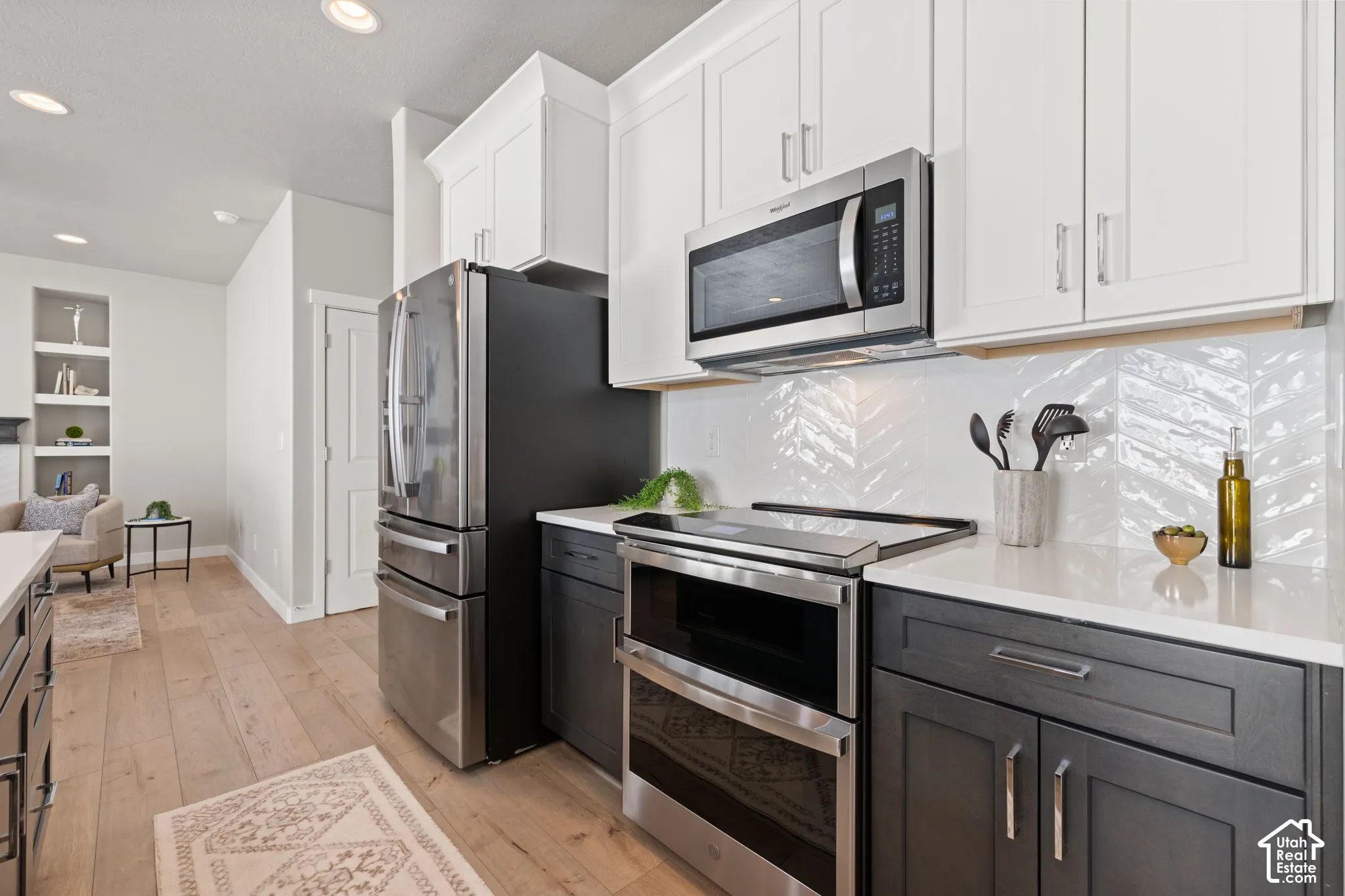 Gourmet kitchen featuring stainless steel appliances, two-tone cabinetry, quartz countertops, and chevron tile backsplash