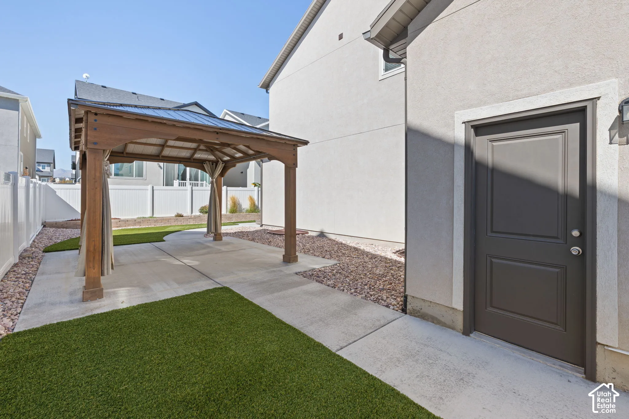 Backyard featuring a wood pergola with a metal roof, concrete patio, artificial turf, and decorative rock landscaping