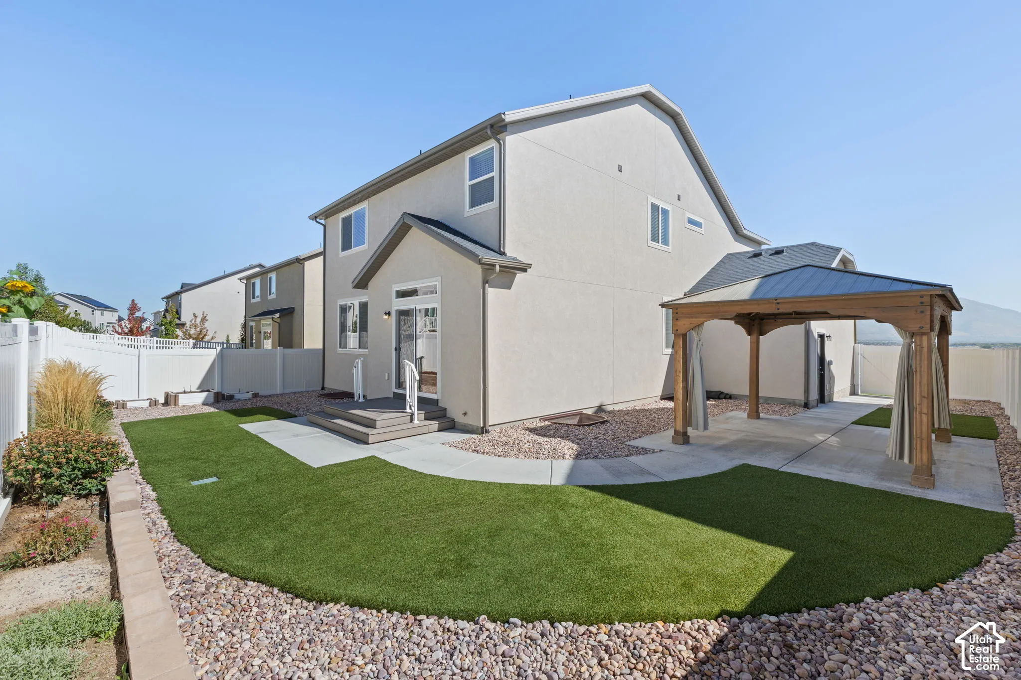 Expansive backyard featuring a manicured artificial turf lawn, a concrete patio, a wooden pergola, and a white privacy fence