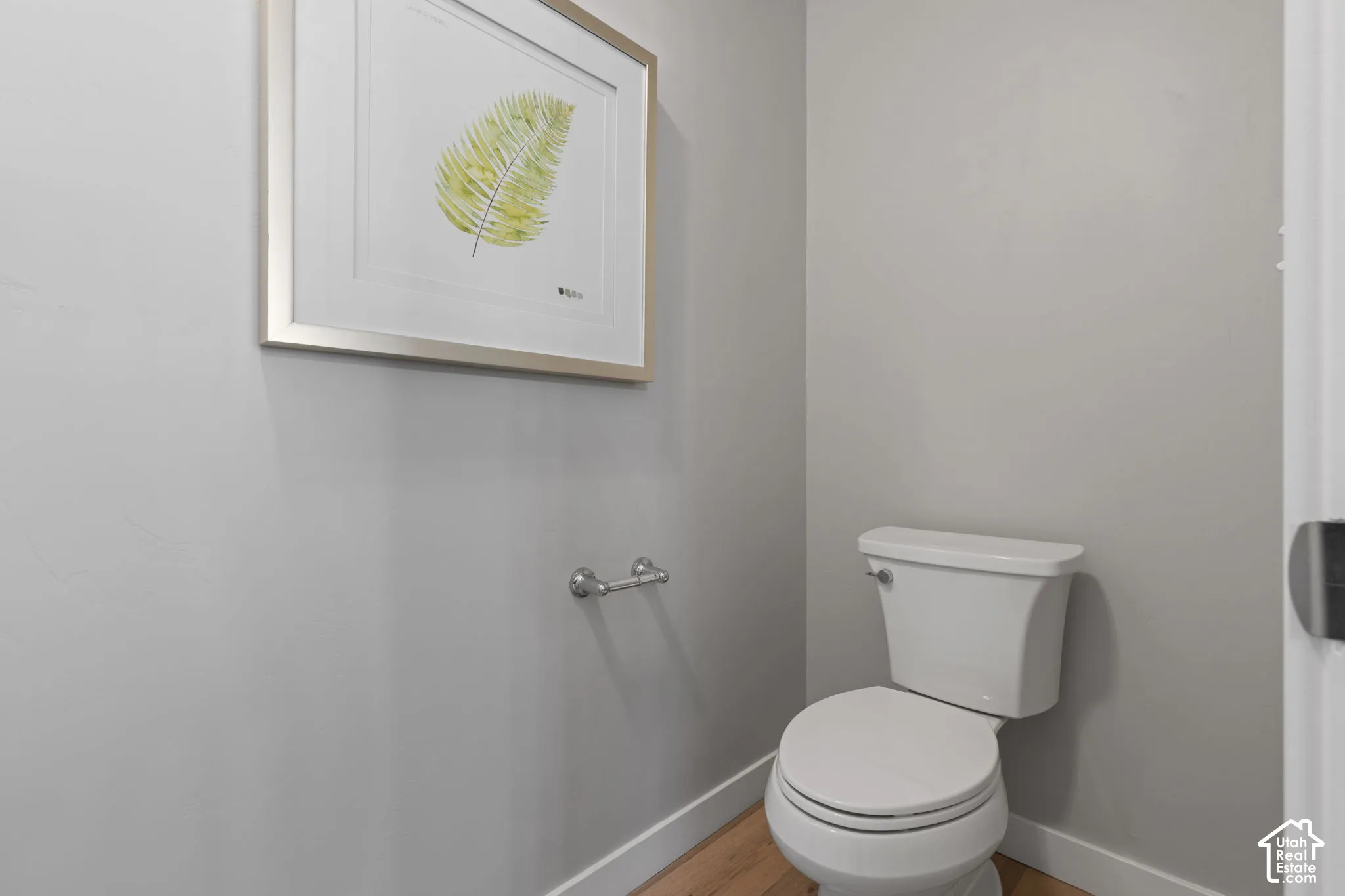 White toilet, wood-finish flooring, light gray wall paint, and white trim