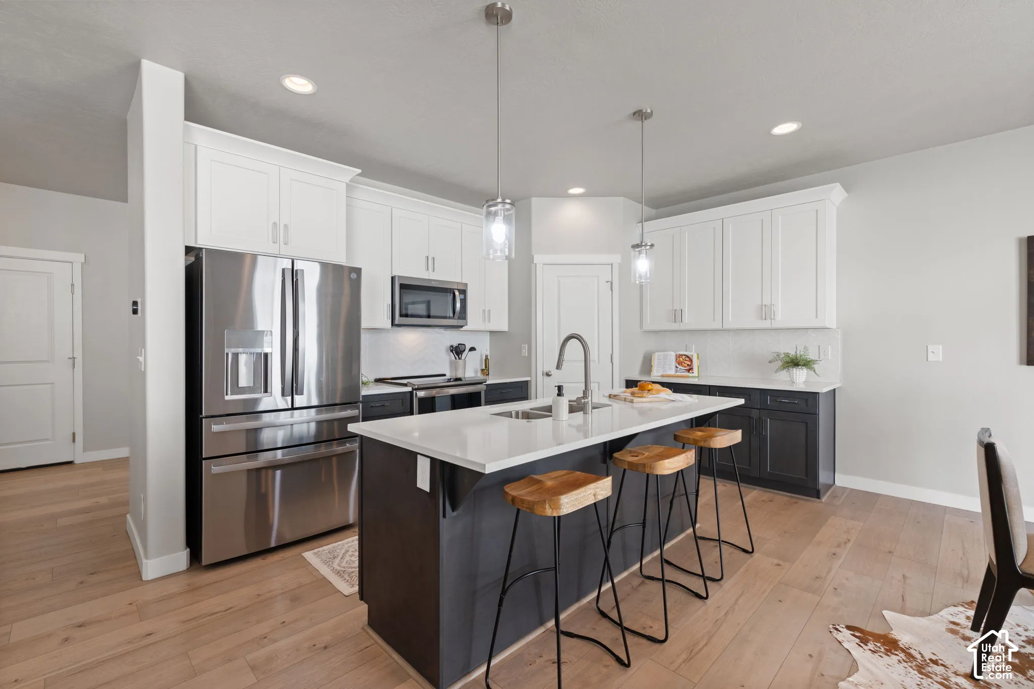 Kitchen featuring an expansive island with countertop seating, stainless steel appliances, a tile backsplash, and wood-finish flooring