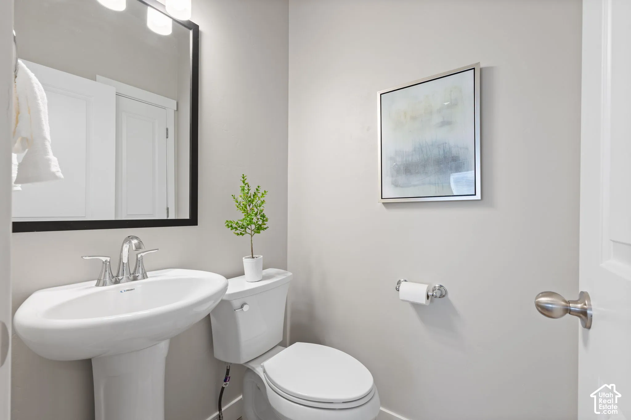 Pedestal sink with chrome faucet, toilet, and framed mirror with integrated lighting