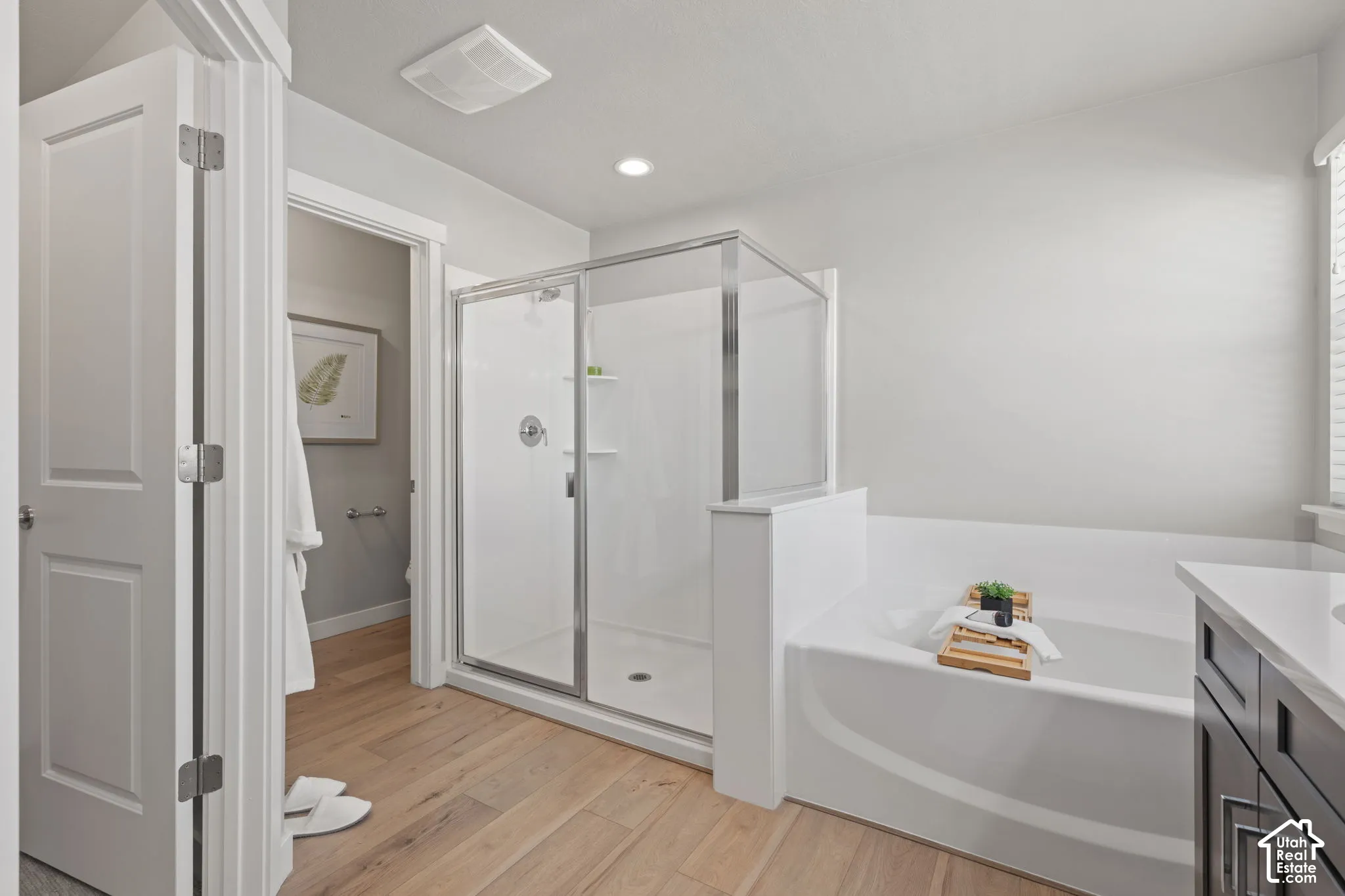 Walk-in shower with glass enclosure, soaking tub, wood-finish flooring, recessed lighting, and a vanity with a light-toned countertop