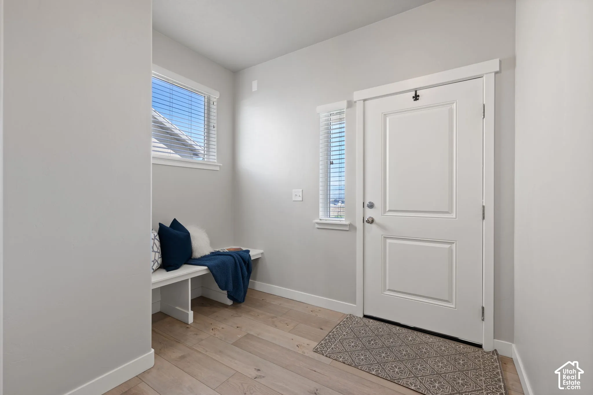 Recessed entry with wood-finish flooring, white paneled door, and natural light from horizontal windows