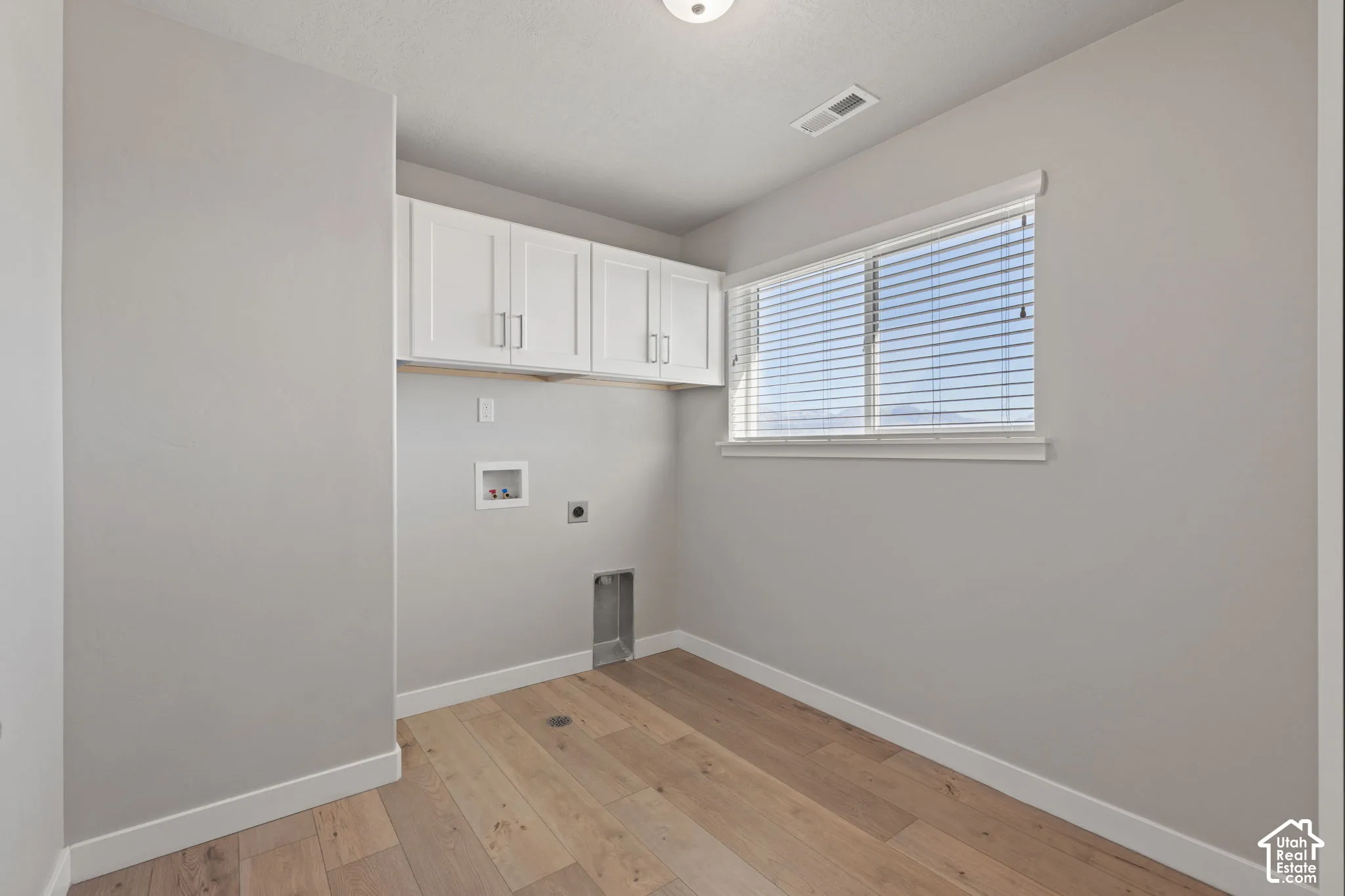 Upper white cabinetry, light wood-finish flooring, and a single window with blinds