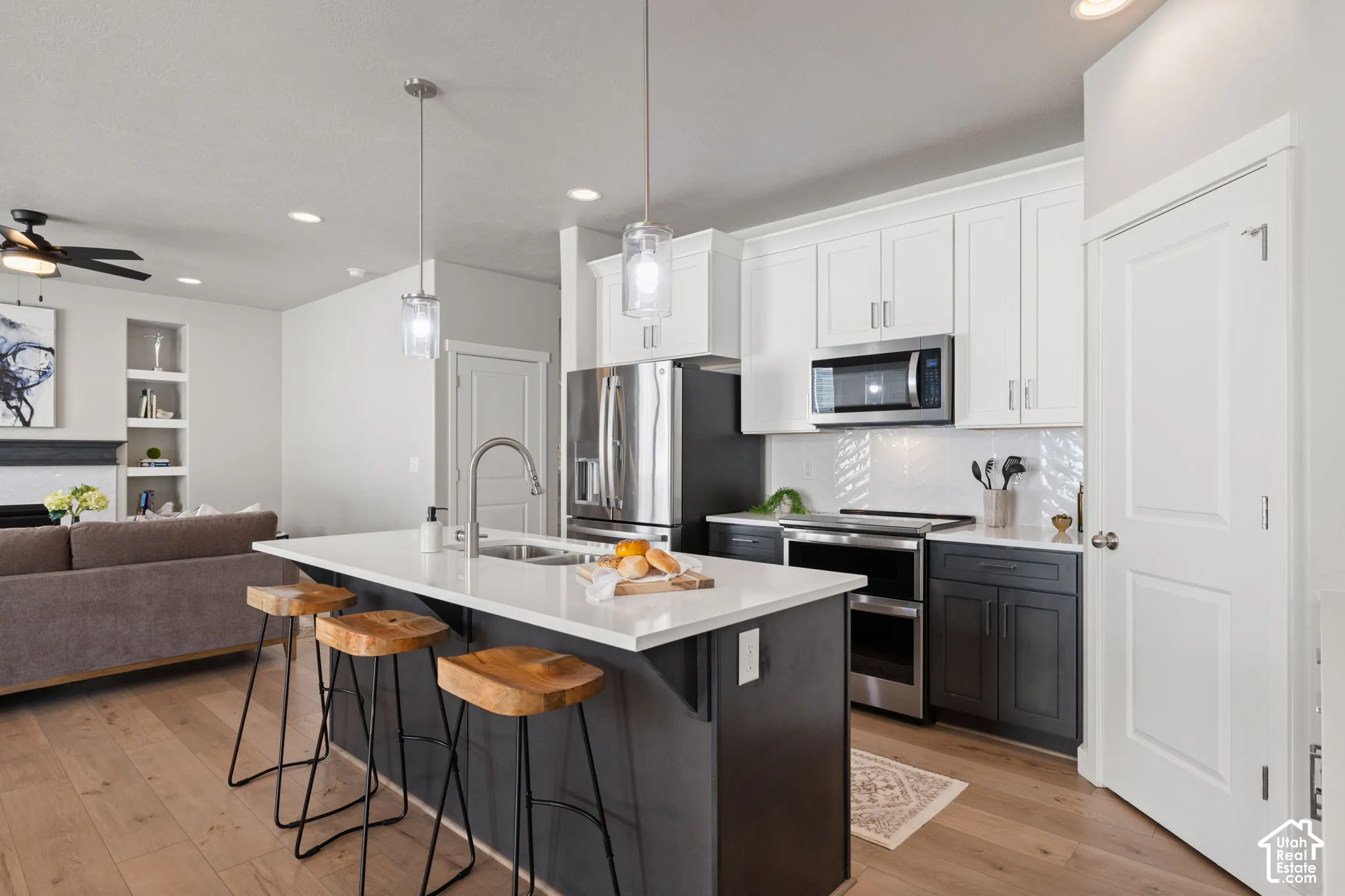 Kitchen island with white countertop, dual pendant lighting, stainless steel appliances, and white shaker-style upper cabinetry