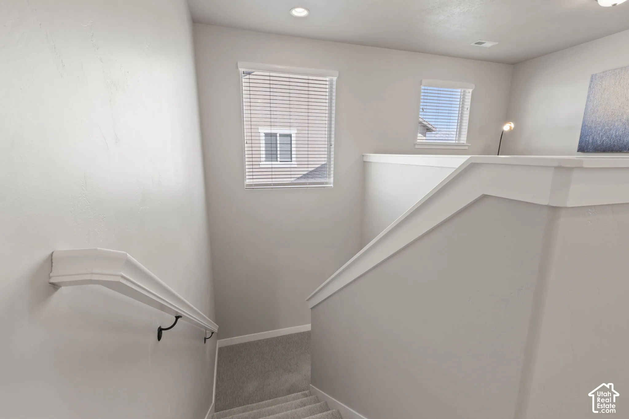 Carpeted staircase with white balustrade, wall-mounted handrail, and recessed lighting