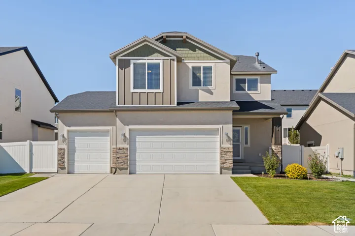 Stucco exterior with stone accents, a multi-car driveway, attached garage, and manicured lawn