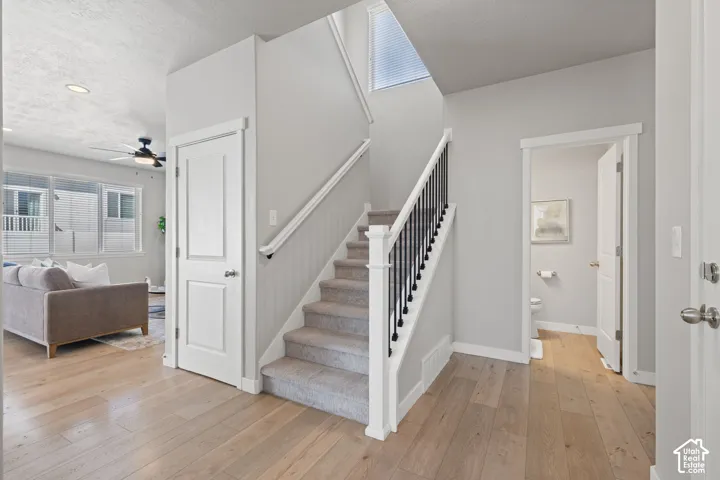 Wood-finish flooring, staircase with carpeted treads and black metal balusters, and a ceiling fan with integrated lighting