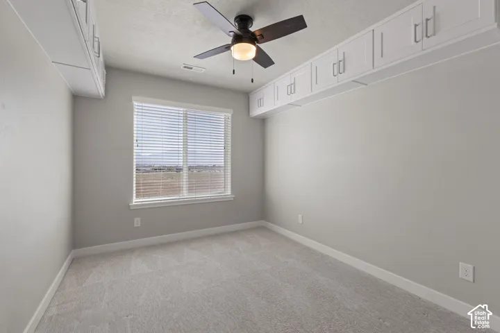 Room featuring light gray carpet, white baseboards, a window with blinds, and white upper cabinetry