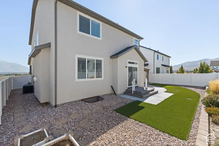 Exterior stucco finish, rear deck with steps, sliding glass patio door, artificial turf lawn, and gravel landscaping with paver stone accents
