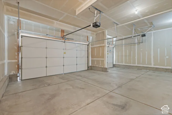 Unfinished garage with a concrete floor, two white panel garage doors, and exposed drywall