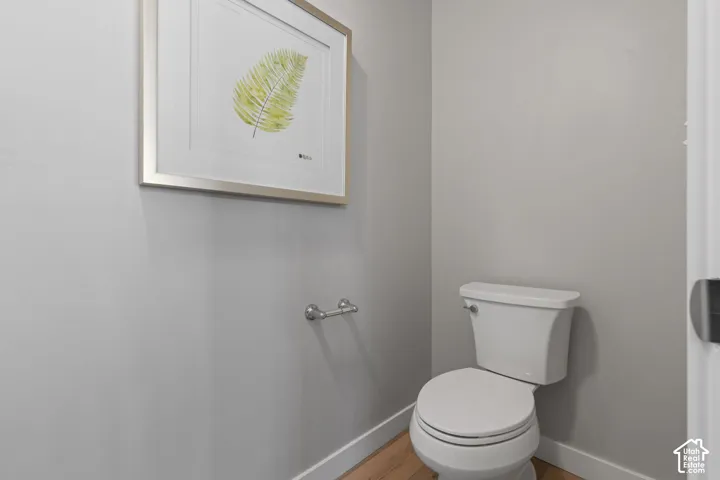White toilet, wood-finish flooring, light gray wall paint, and white trim