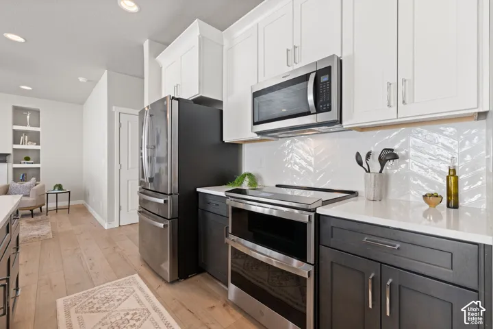 Gourmet kitchen featuring stainless steel appliances, two-tone cabinetry, quartz countertops, and chevron tile backsplash