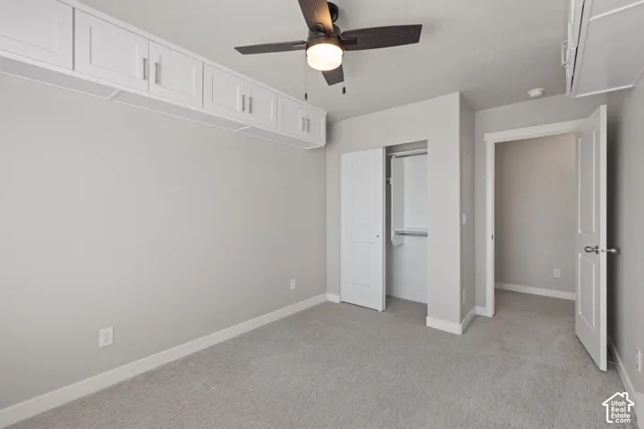 Recessed overhead cabinetry with brushed nickel hardware, ceiling fan with integrated lighting, soft grey wall paint, plush grey carpeting, and a bi-fold door closet