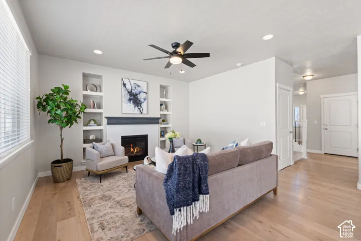Recessed lighting, wood-finish flooring, built-in shelving, a tiled fireplace with a dark mantel, and a ceiling fan