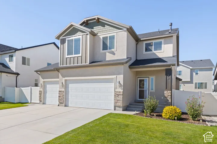 Stucco exterior with stone accents, attached three-car garage, white fencing, and a manicured lawn