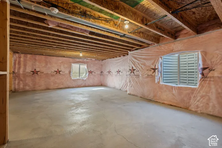 Unfinished basement with exposed ceiling joists, concrete flooring, and two egress windows