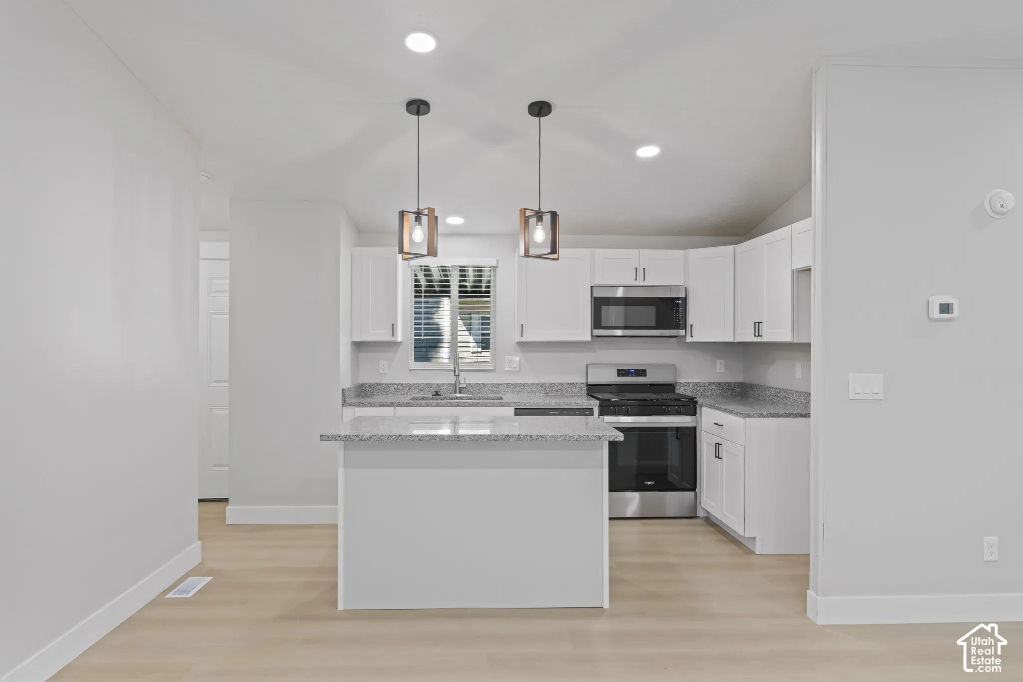 Kitchen featuring white cabinetry, stainless steel appliances, granite-style countertops, wood-finish flooring, and recessed lighting