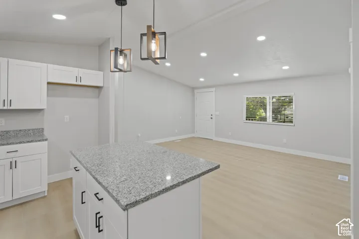 Kitchen island with stone-finish countertop, white cabinetry with black hardware, wood-finish flooring, recessed lighting, and decorative pendant light fixtures
