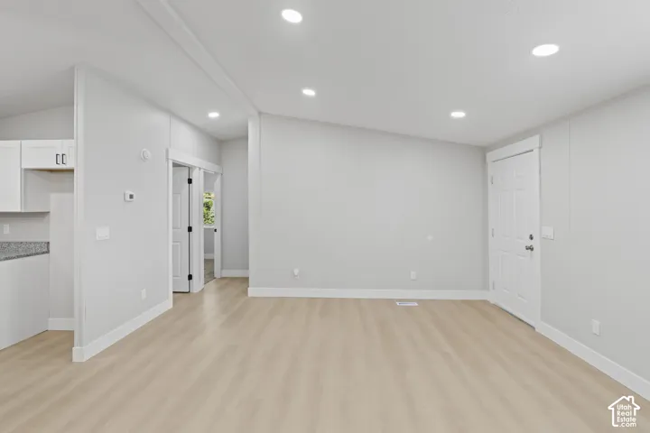 Recessed lighting throughout, wood-finish flooring, white trim details, white kitchen cabinetry, and a granite-finish countertop