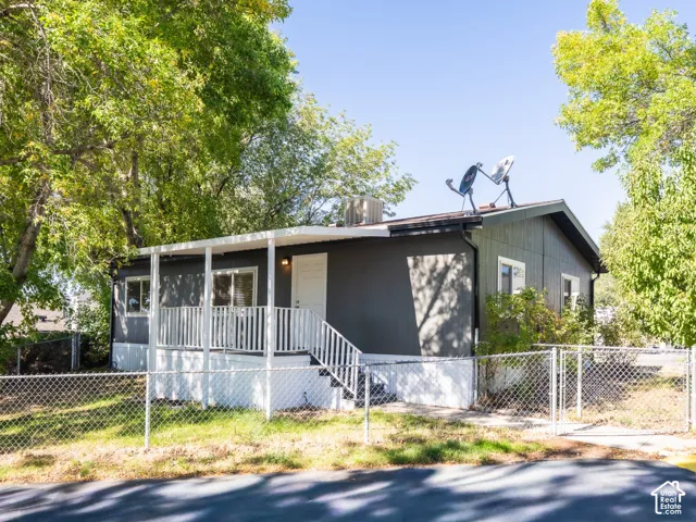 Exterior facade featuring dark-toned siding, a covered front porch with white railing, and a chain-link fenced perimeter