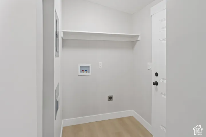 Laundry area featuring light wood-finish flooring, a white utility shelf, and laundry hookups