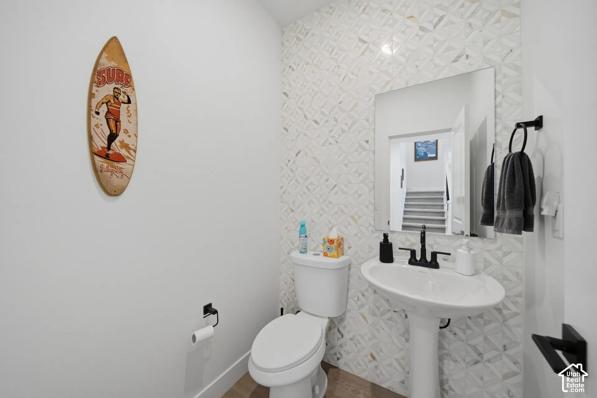 Pedestal sink with a matte black faucet, wall-mounted mirror, and decorative tiled accent wall