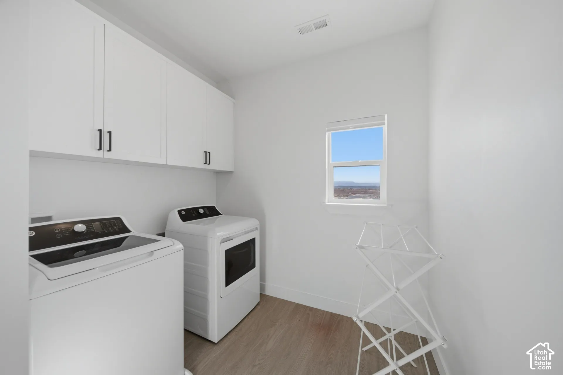 White upper cabinetry with dark hardware, a single window, and light wood-finish flooring