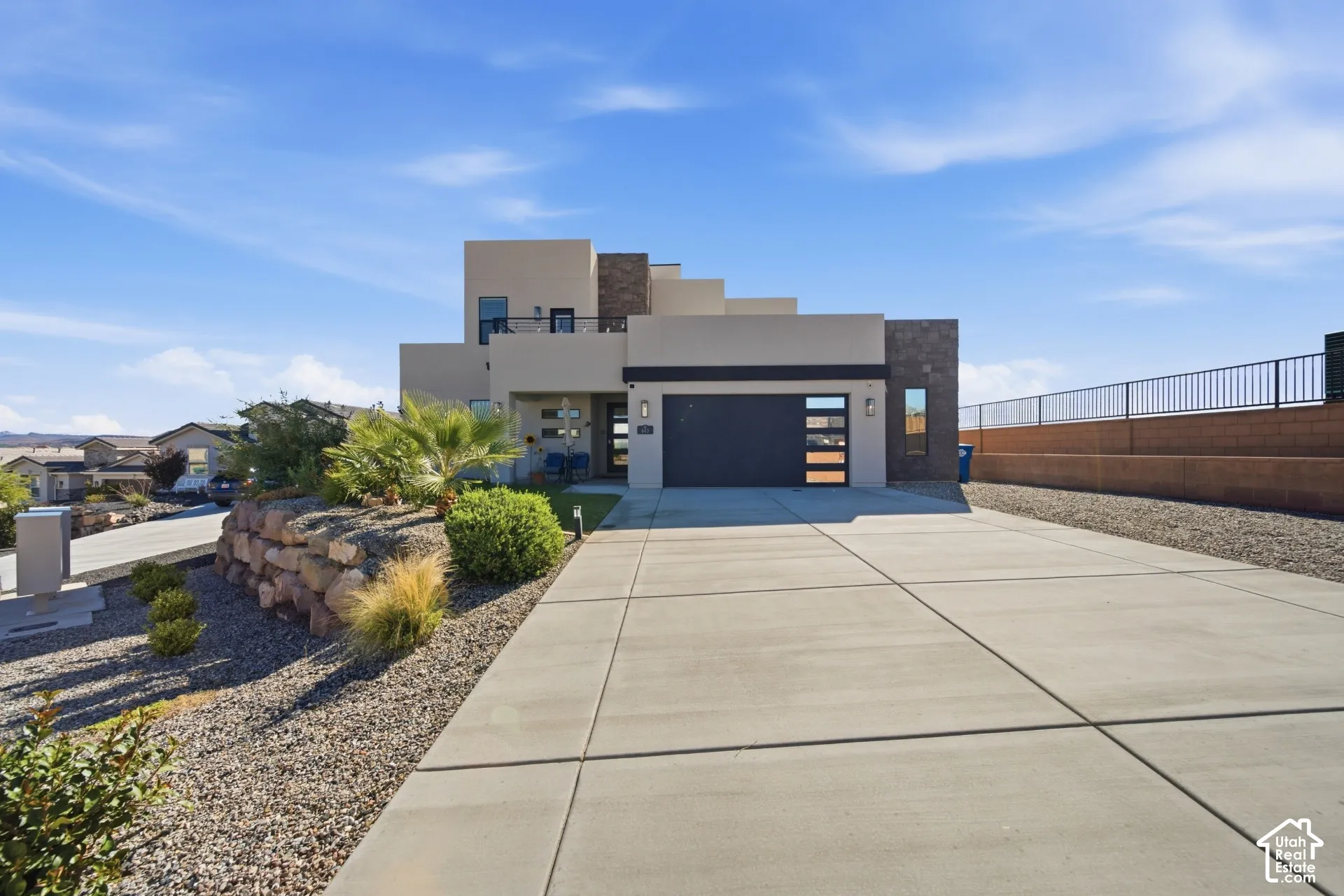 Contemporary exterior with multi-level design, attached garage with frosted glass panels, expansive concrete driveway, and a retaining wall with desert landscaping