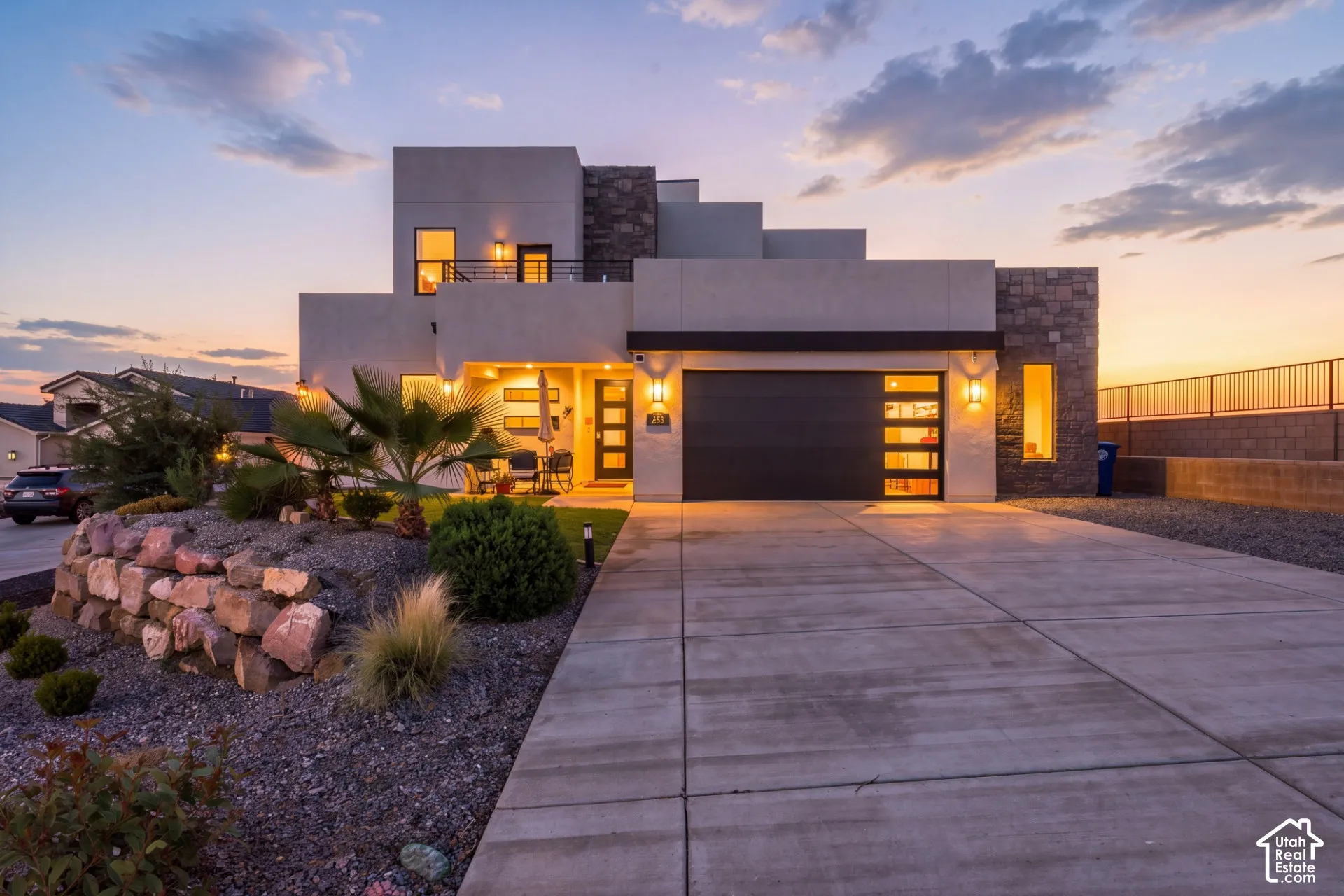 Modern architectural design featuring stacked stone accents, a concrete driveway, and xeriscape landscaping