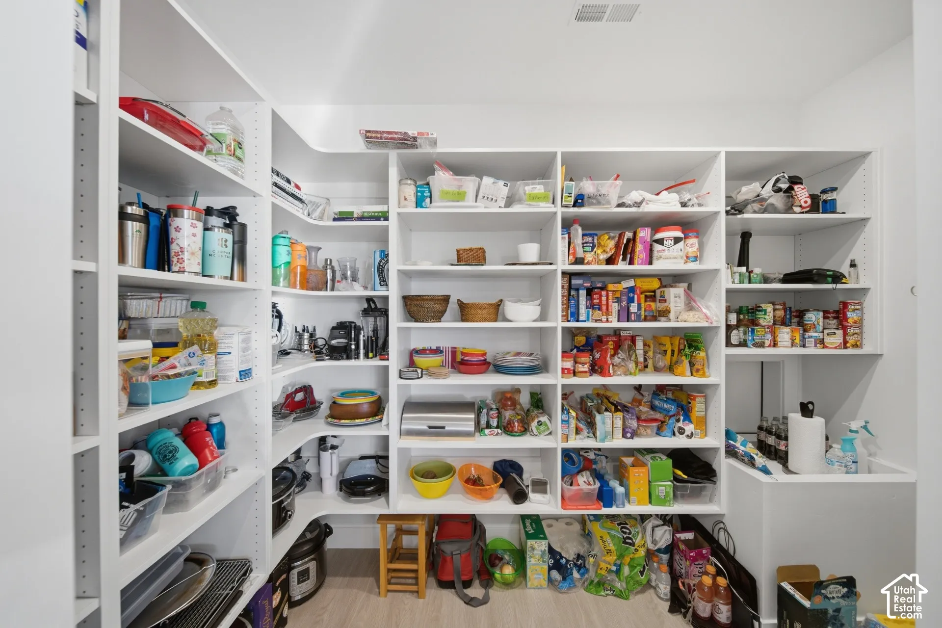 Expansive walk-in pantry featuring abundant built-in shelving, white cabinetry, and light wood-finish flooring