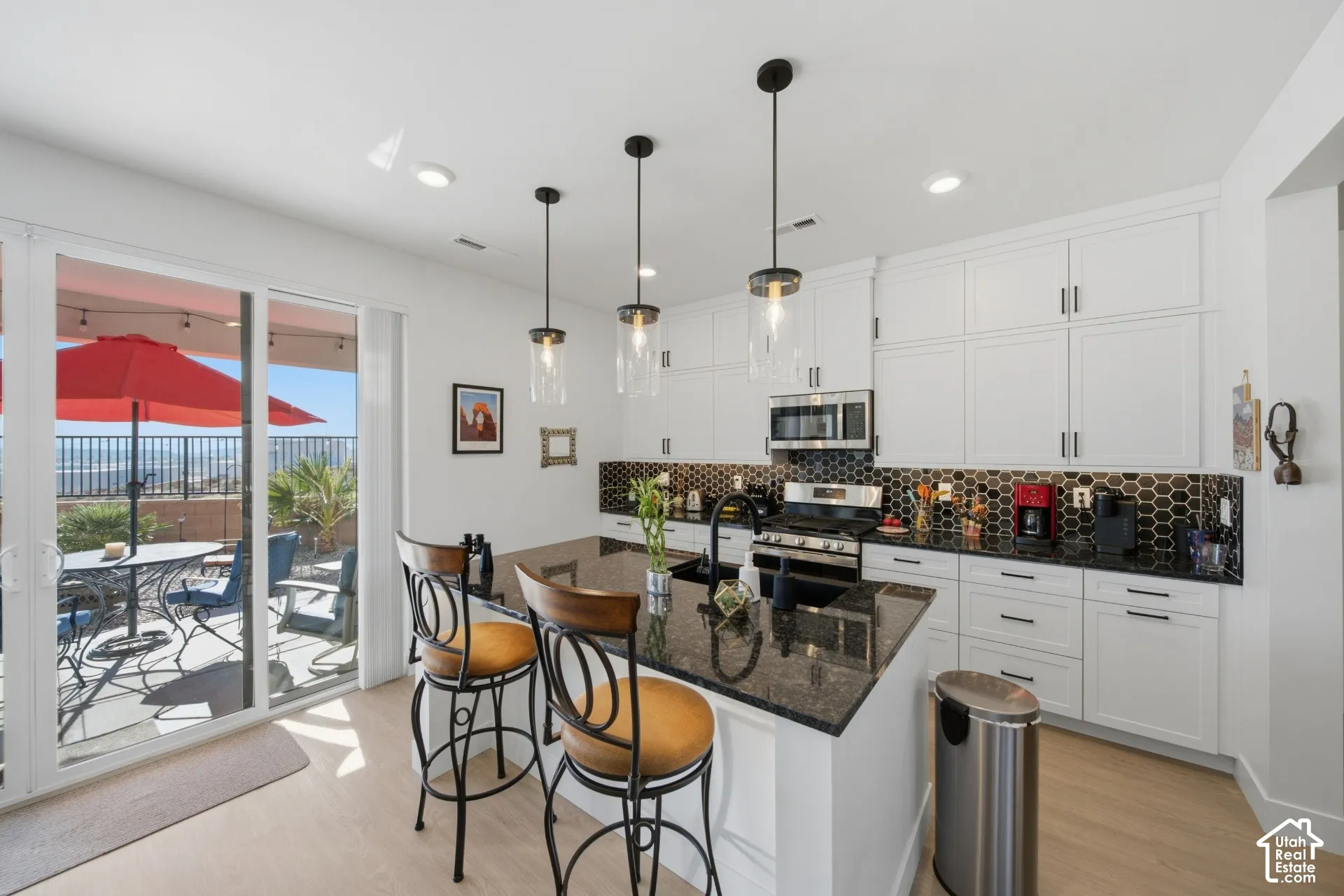 Kitchen featuring white shaker-style cabinetry, black granite countertops, a black hexagonal tile backsplash, stainless steel appliances, and pendant lighting