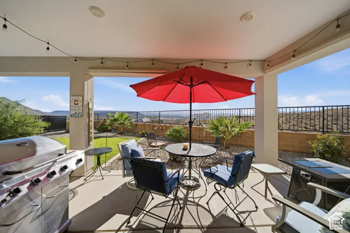Covered patio with string lighting, concrete flooring, and a low-maintenance landscape featuring a block wall and black metal fencing