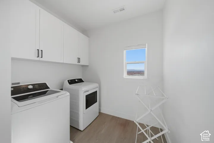 White upper cabinetry with dark hardware, a single window, and light wood-finish flooring