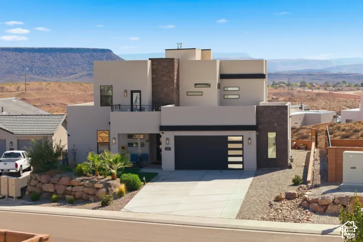 Modern architectural design featuring varied rectangular windows, a prominent garage with opaque glass inserts, a second-story balcony with metal railing, and integrated stone facade elements