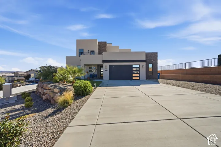 Contemporary exterior with multi-level design, attached garage with frosted glass panels, expansive concrete driveway, and a retaining wall with desert landscaping