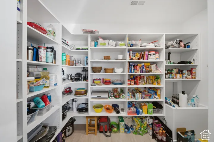 Expansive walk-in pantry featuring abundant built-in shelving, white cabinetry, and light wood-finish flooring