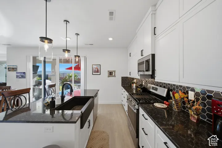 White cabinetry with black hardware, dark countertops, and a black hexagonal tile backsplash