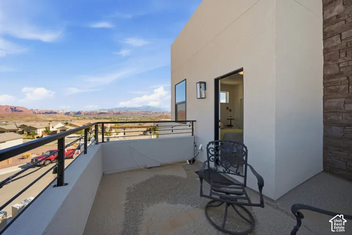 Exterior balcony with a metal railing, desert and mountain backdrop, stucco exterior, stone accent wall, and an exterior wall light fixture