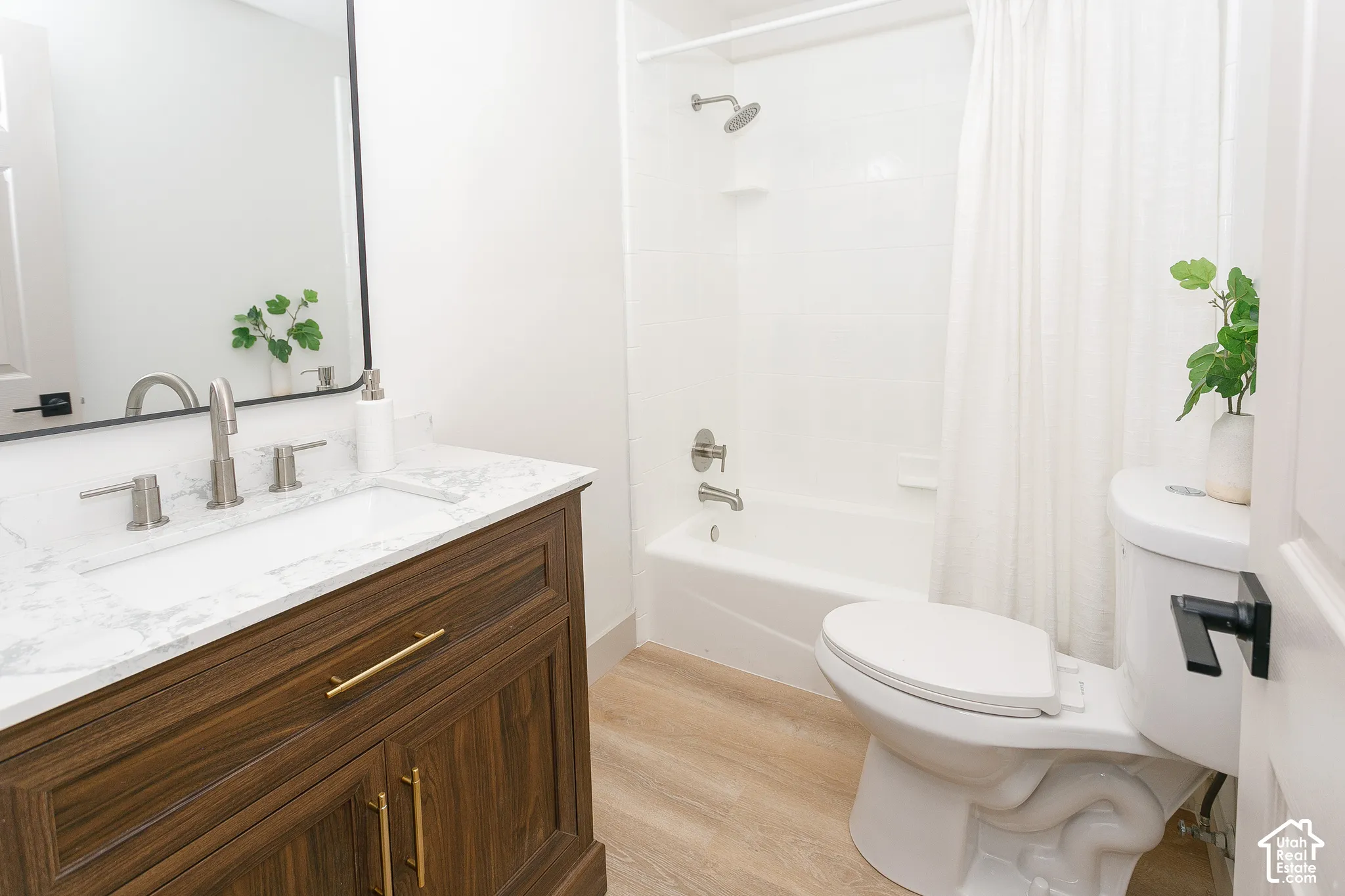 Wood-finish flooring, a white vanity with a rectangular undermount sink, a white countertop with gray veining, and a white tub with an integrated shower
