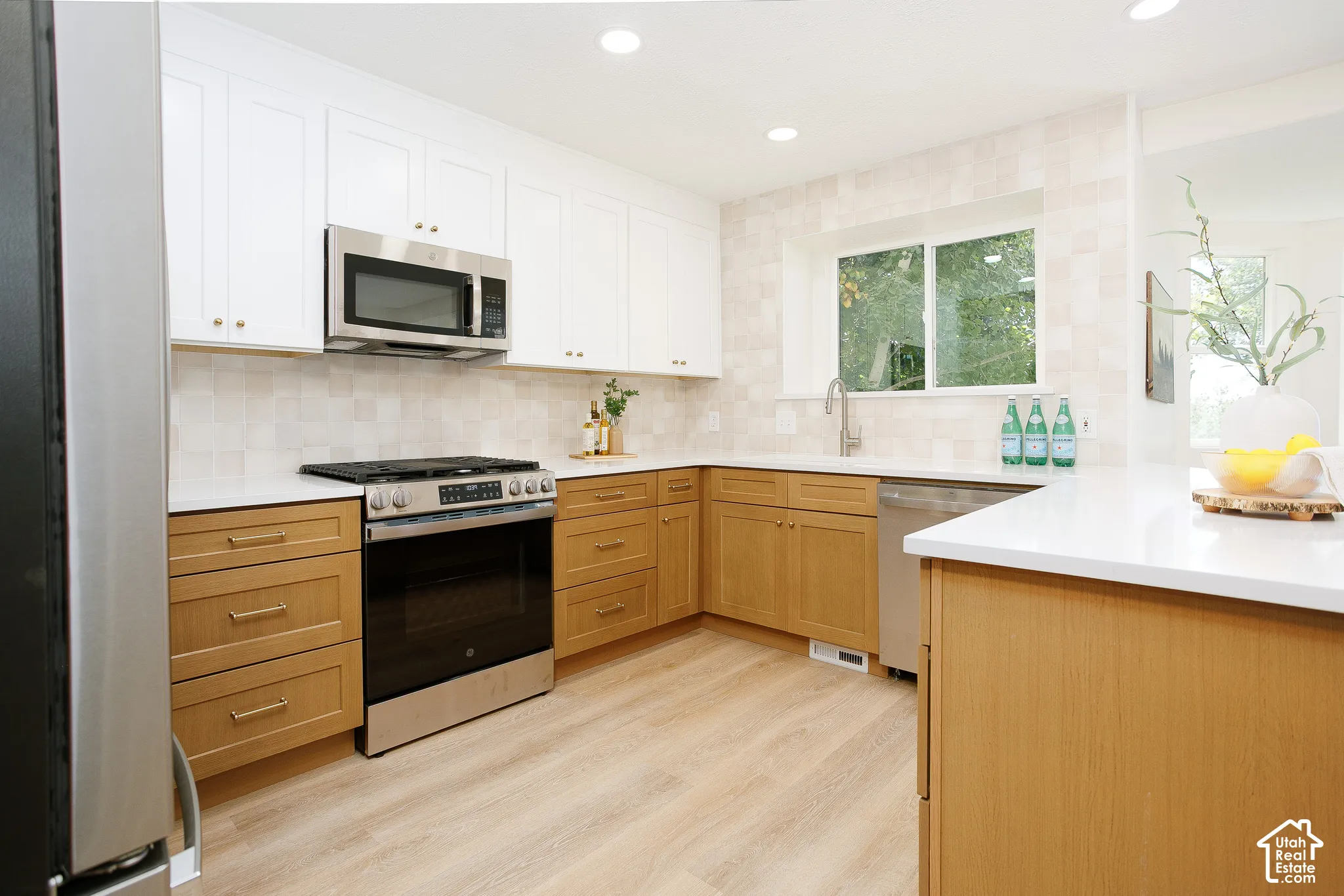 Modern kitchen featuring two-tone cabinetry, stainless steel appliances, light-toned wood-finish flooring, and recessed lighting