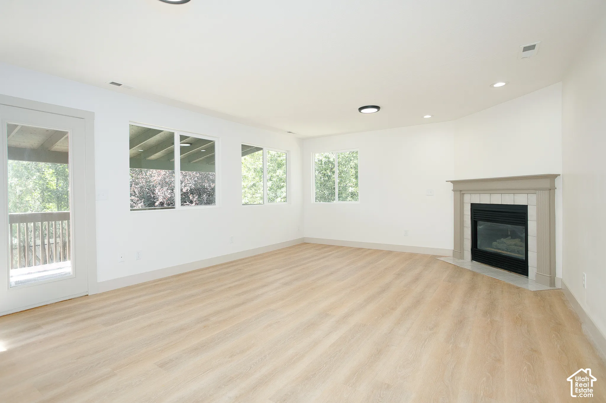 Spacious room featuring wood-finish flooring, a contemporary fireplace with a tiled surround, recessed lighting, and multiple windows